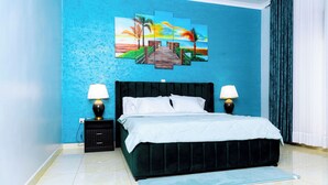 A bedroom with a bed, two bedside tables, a nightstand, a blue wall, and a large painting.