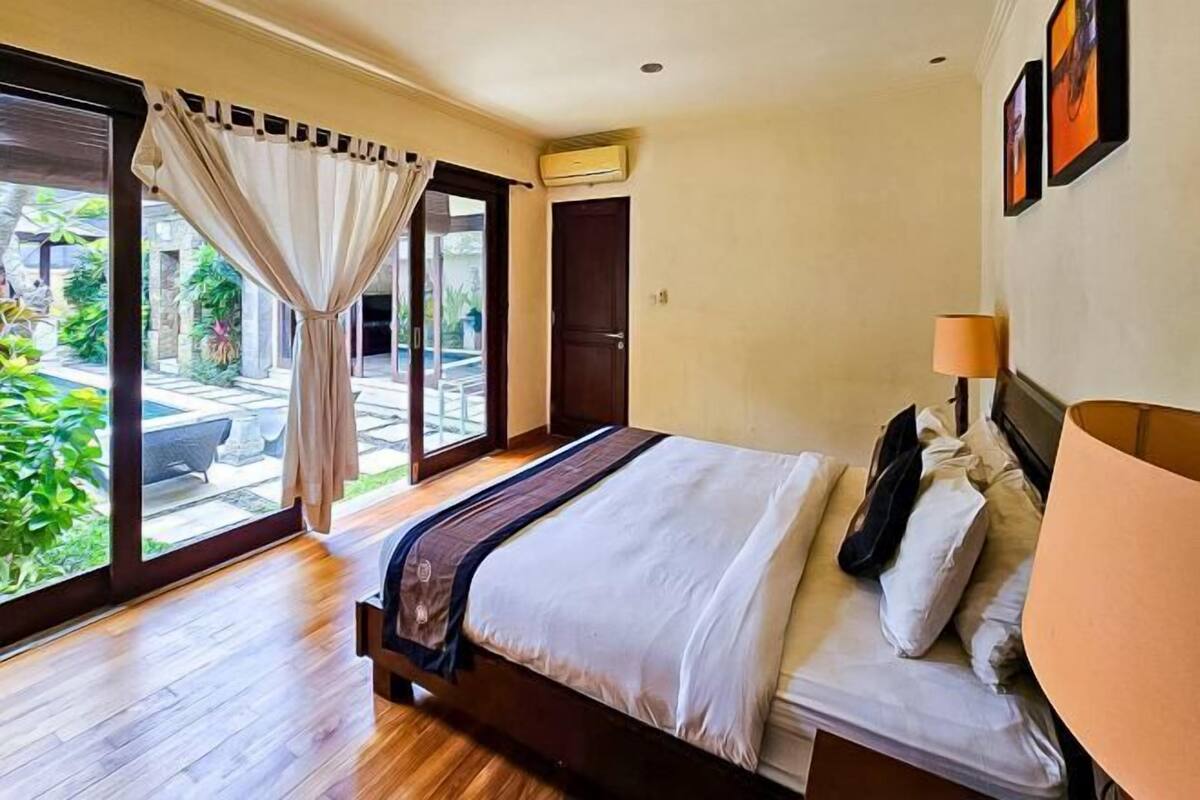 A bedroom with a bed, a window with curtains, a door, and an air conditioning unit.