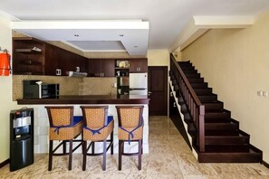 A kitchen with a bar area, three bar stools, a microwave, and a refrigerator.