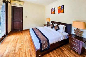 A hotel room with a wooden floor, a bed with a headboard, two bedside tables with lamps, and a door. - The Lavana Villa Bukit Jimbaran (2 Bedroom Villa with Private Pool - Minimum Stay 3 Nights) (Bali)