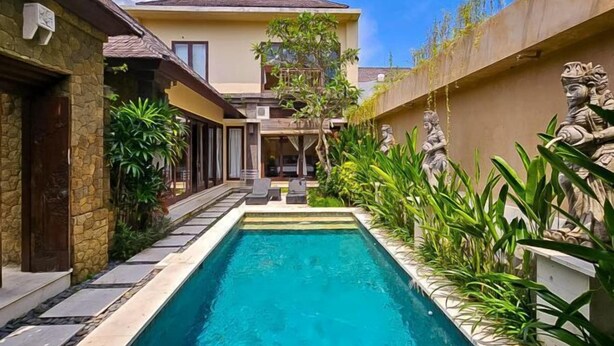 A rectangular swimming pool with a stone border, surrounded by lush greenery and statues. - The Lavana Villa Bukit Jimbaran (2 Bedroom Villa with Private Pool - Minimum Stay 3 Nights) (Bali)