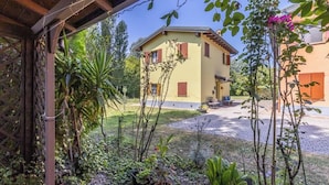 Un bâtiment jaune avec un jardin à l’avant, une pergola en bois et un ciel dégagé.