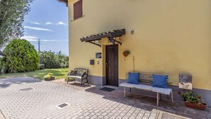Un bâtiment jaune avec une porte, un banc et un petit espace jardin avec des plantes.