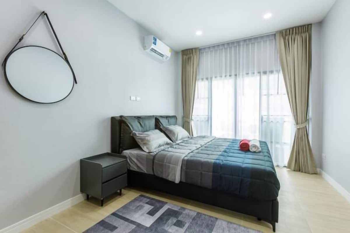 Une chambre à coucher comprenant un lit, une table de chevet, un climatiseur fixé au mur et une fenêtre avec des rideaux.