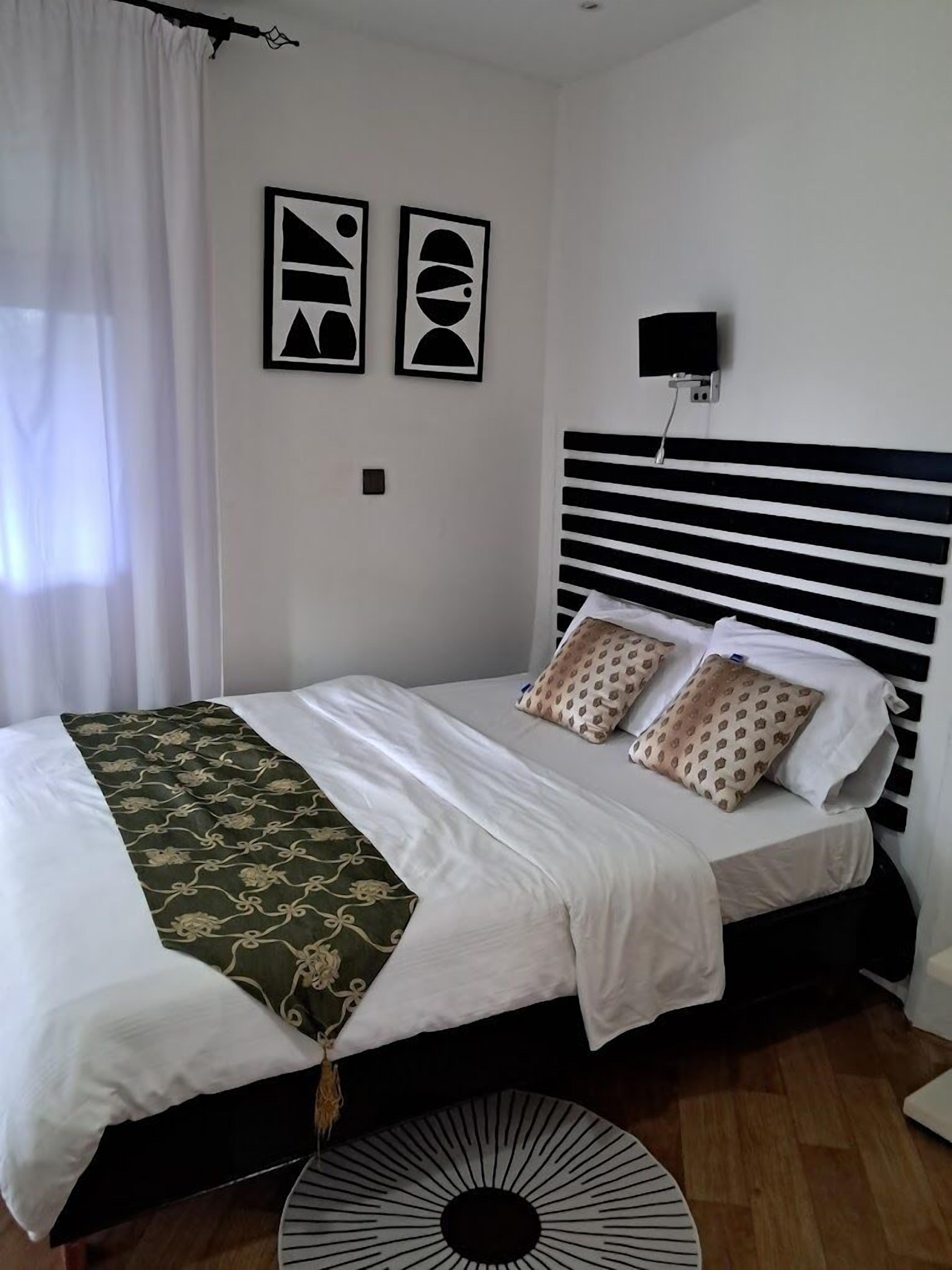 A neatly made bed with a patterned throw, a black and white headboard, and two wall-mounted abstract art pieces.