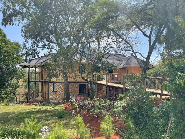 Une maison à deux étages avec une façade en pierre, une terrasse en bois et un jardin agrémenté de diverses plantes.