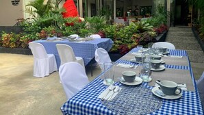 An outdoor dining area with checkered tablecloths, white chairs, and a variety of plants and flowers. - OYO 1177 The Great Molave (Alfonso)