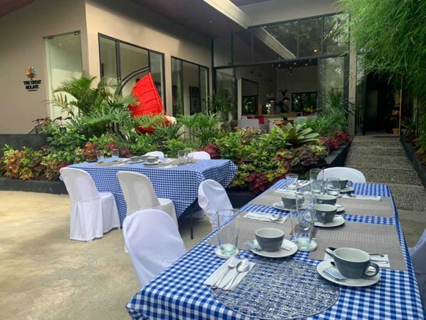 An outdoor dining area with checkered tablecloths, white chairs, and a variety of plants and flowers.