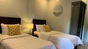 A hotel room with two beds, each with a white quilted bedspread and decorative pillows. There is a bedside table with a lamp, and a wall-mounted decorative piece above the beds. - OYO 1177 The Great Molave (Alfonso)