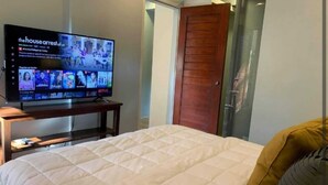 A hotel room with a bed, a TV displaying a show, and a wooden door. - OYO 1177 The Great Molave (Alfonso)
