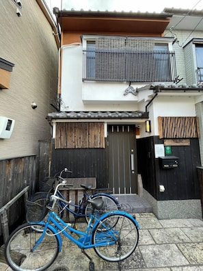 A blue bicycle parked in front of a building with a black gate and a small table. - Fushimi Inari House (Kyoto)