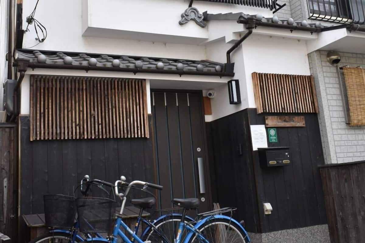 Un bâtiment à deux étages, avec un portail noir, un vélo bleu et une clôture en bois.
