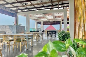 Un área de comedor al aire libre con mesas y sillas, un muro de piedra y vista al océano.