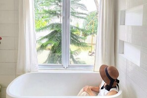 A bathtub with a view of palm trees outside. - Floraison Living Villa Yogyakarta (Ngaglik)