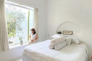 A bedroom with a large bed, a window with curtains, and a wall-mounted picture frame. - Floraison Living Villa Yogyakarta (Ngaglik)