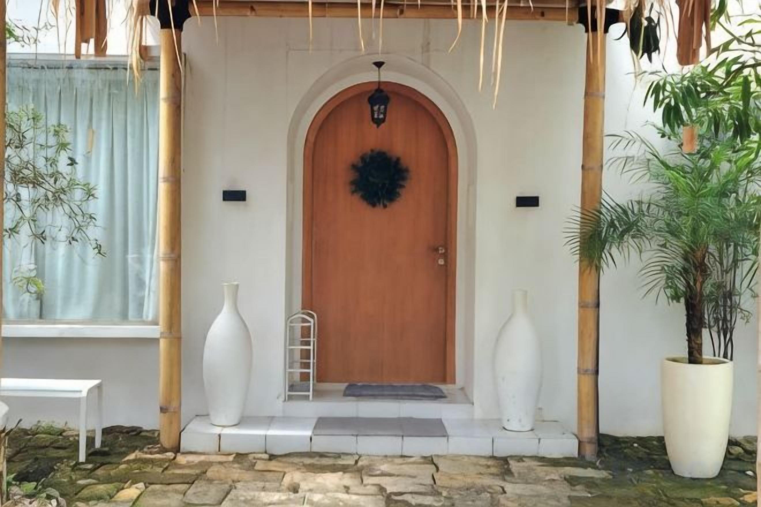 A wooden door with a circular wreath, a white bench, and a large potted plant.