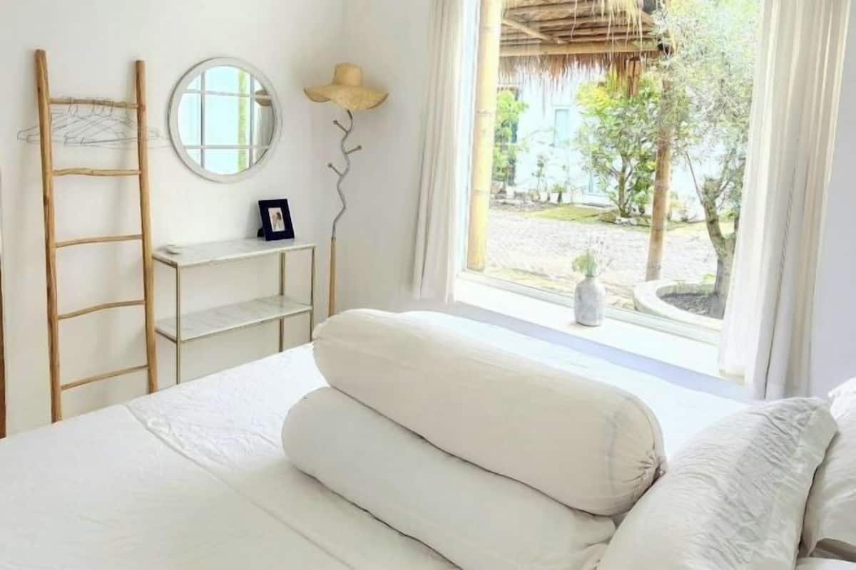 A bedroom with a bed, a ladder, a shelf, a mirror, and a view of the outside.