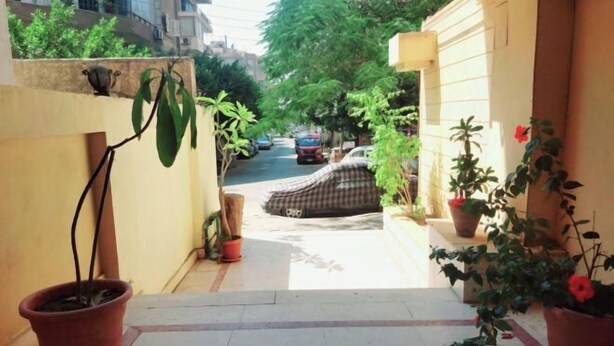 A narrow pathway leading to a parked car, flanked by potted plants and a building facade. - Jessy Residential Apartment (Cairo)