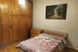 A bedroom with a bed, a wooden wardrobe, a small bedside table, and a painting on the wall. - Jessy Residential Apartment (Cairo)