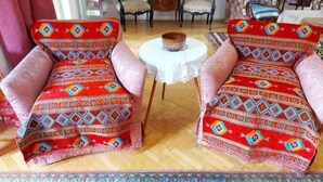 Two armchairs with colorful patterned upholstery, a small round table with a white tablecloth, and a patterned rug on a wooden floor. - Jessy Residential Apartment (Cairo)