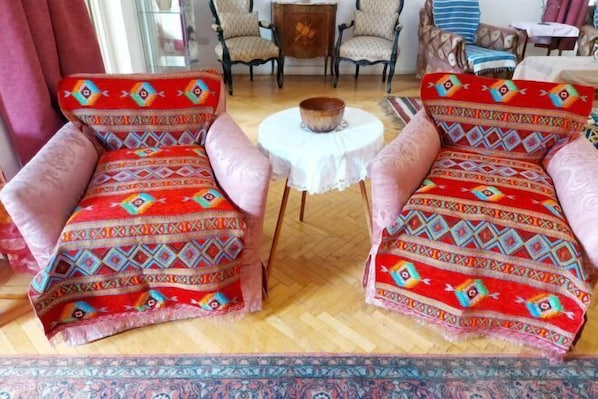 Two armchairs with colorful patterned upholstery, a small round table with a white tablecloth, and a patterned rug on a wooden floor.