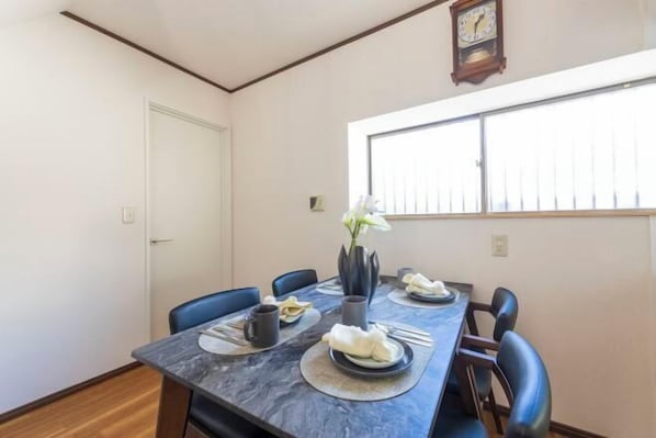 A dining area with a marble table, blue chairs, a vase with flowers, and a clock on the wall.