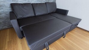 A modern black sofa with a flat surface and a footrest, positioned against a textured wall and wooden flooring. - Ikebukuro 15min｜Family House｜8Guests (Tokyo)