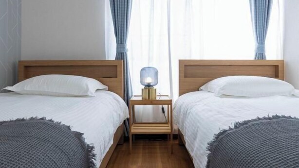 A hotel room with two single beds, a bedside table with a lamp, and a window with curtains. - Ikebukuro 15min｜Family House｜8Guests (Tokyo)