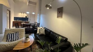 A modern living room with a sofa, armchair, and coffee table. There is a dining area with chairs and a table in the background. - W. House for group, Cozy Loft near Suvarnabhumi Airport (Bangkok)