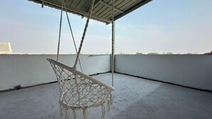 A white macrame hanging chair on a concrete floor with a metal roof and a view of a distant building. - W. House for group, Cozy Loft near Suvarnabhumi Airport (Bangkok)