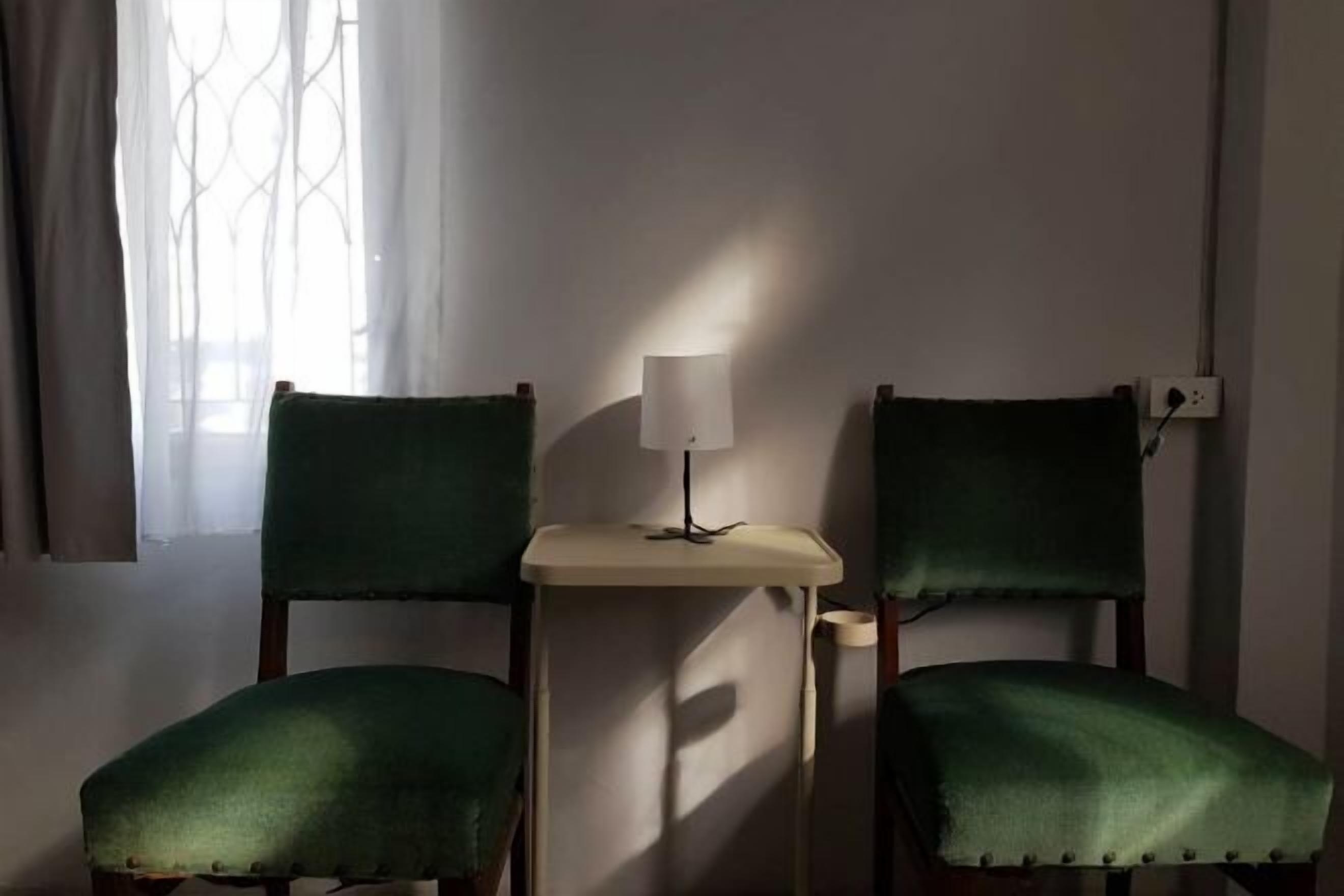 A room with two green upholstered chairs and a small table with a lamp.