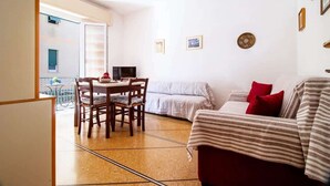 Ein gemütliches Wohnzimmer mit einer Couch, einem Esstisch mit Stühlen und einem Fernseher. Ein Balkon mit Tisch und Stühlen ist vorhanden.