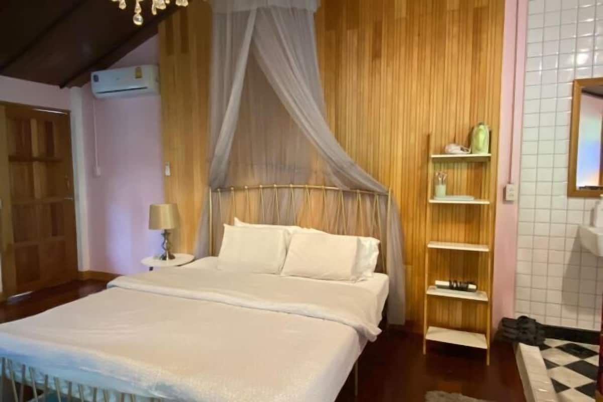 A bedroom with a bed, a nightstand, a shelf, and a wooden wardrobe.