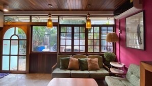 A cozy room with a wooden ceiling, a green sofa with cushions, a small table, and a window with a view of greenery outside. - T-House BKK 2floors near BTS with Swimming pool and Free Wifi (Bangkok)