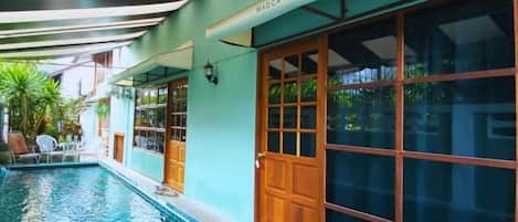 Una piscina junto a un edificio con grandes ventanales y un cartel que dice 'MADCAT BANKOK'.