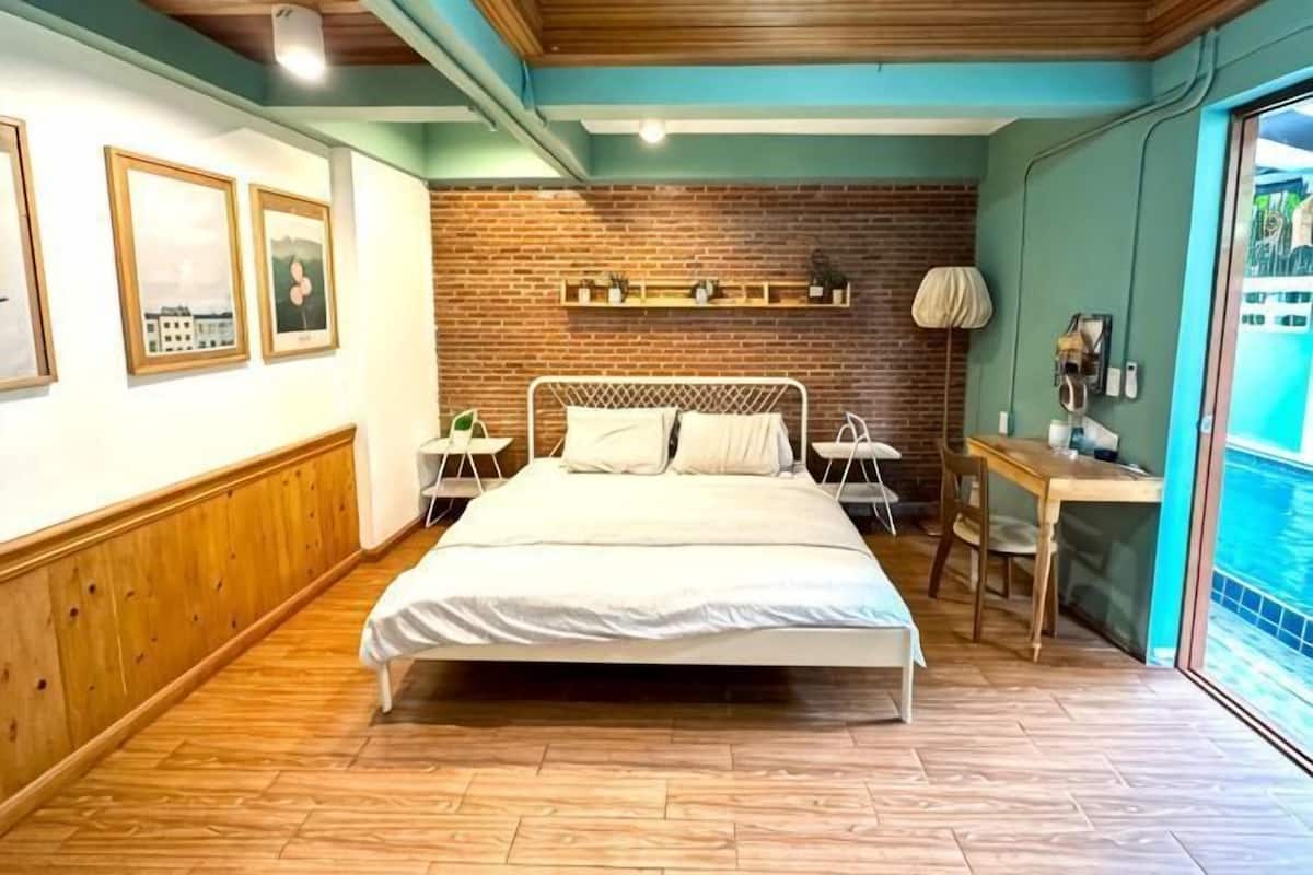 A bedroom with a bed, bedside tables, a desk, and a view of a pool.