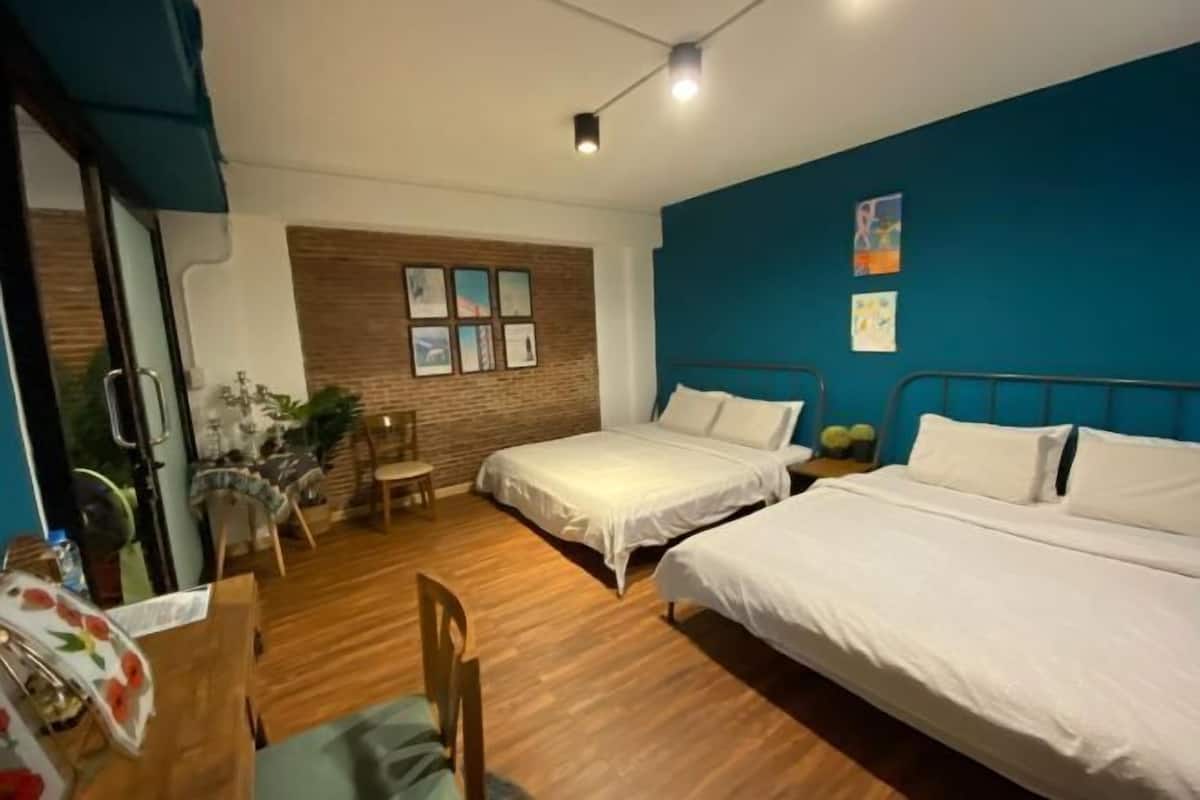 A hotel room with two beds, a wooden floor, a brick accent wall, and a view of the outdoors.