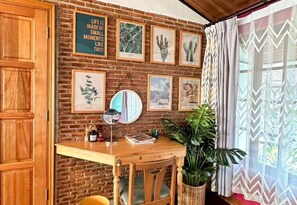 Una habitación con pared de ladrillo, un escritorio de madera, una silla, una planta en maceta y cuadros enmarcados.
