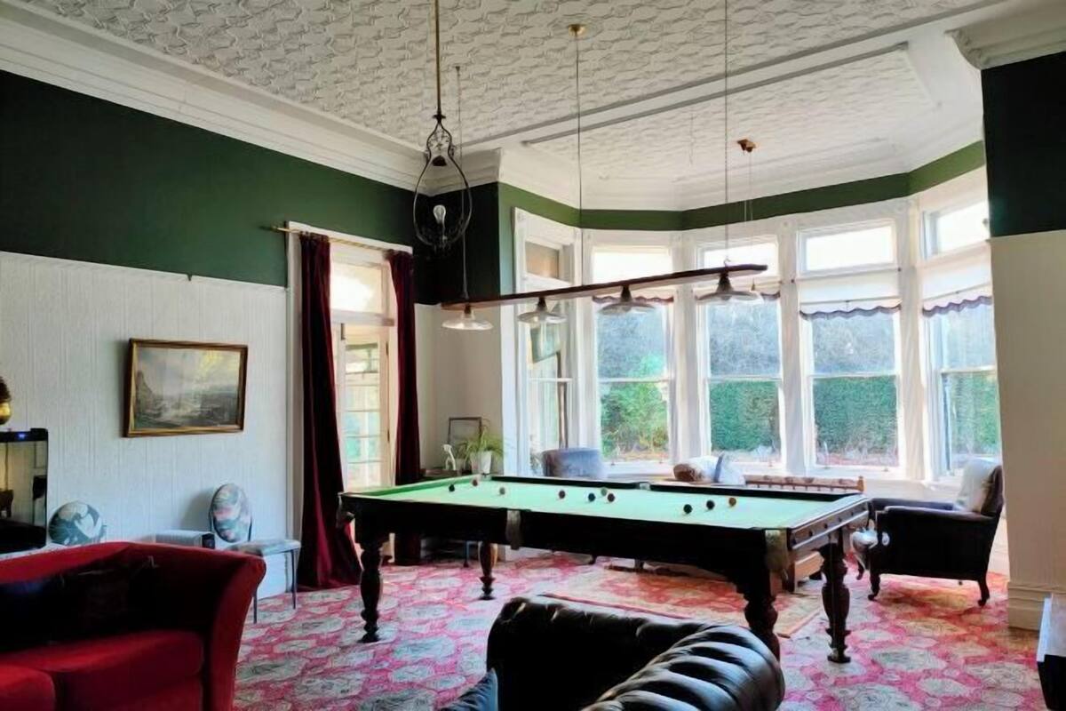 A room with a pool table, a red sofa, and a billiard table.