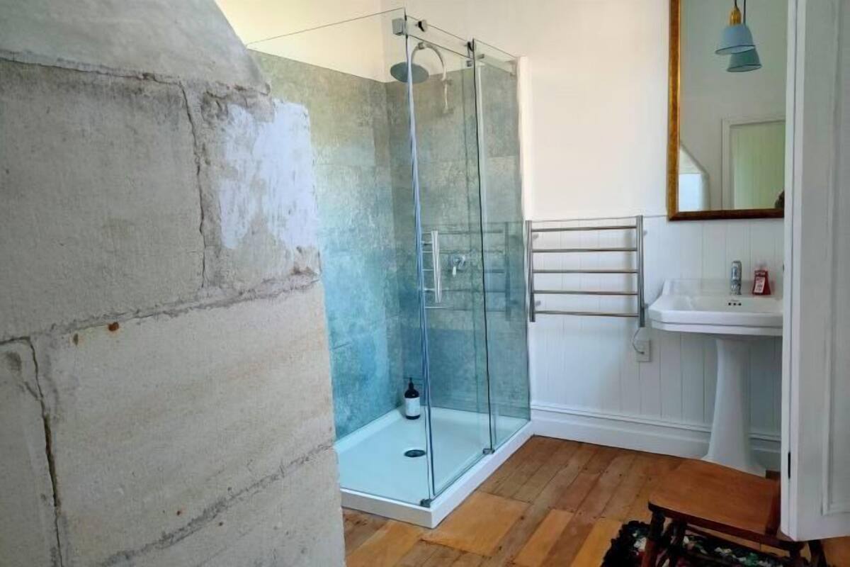 A bathroom with a glass shower enclosure, a white sink, and a mirror.