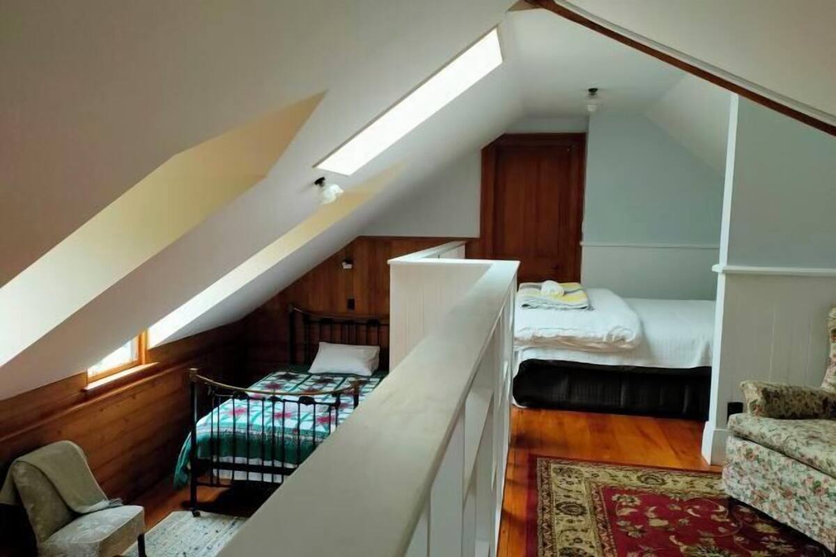 A loft bedroom with a sloped ceiling, a bunk bed, a chair, and a small desk.