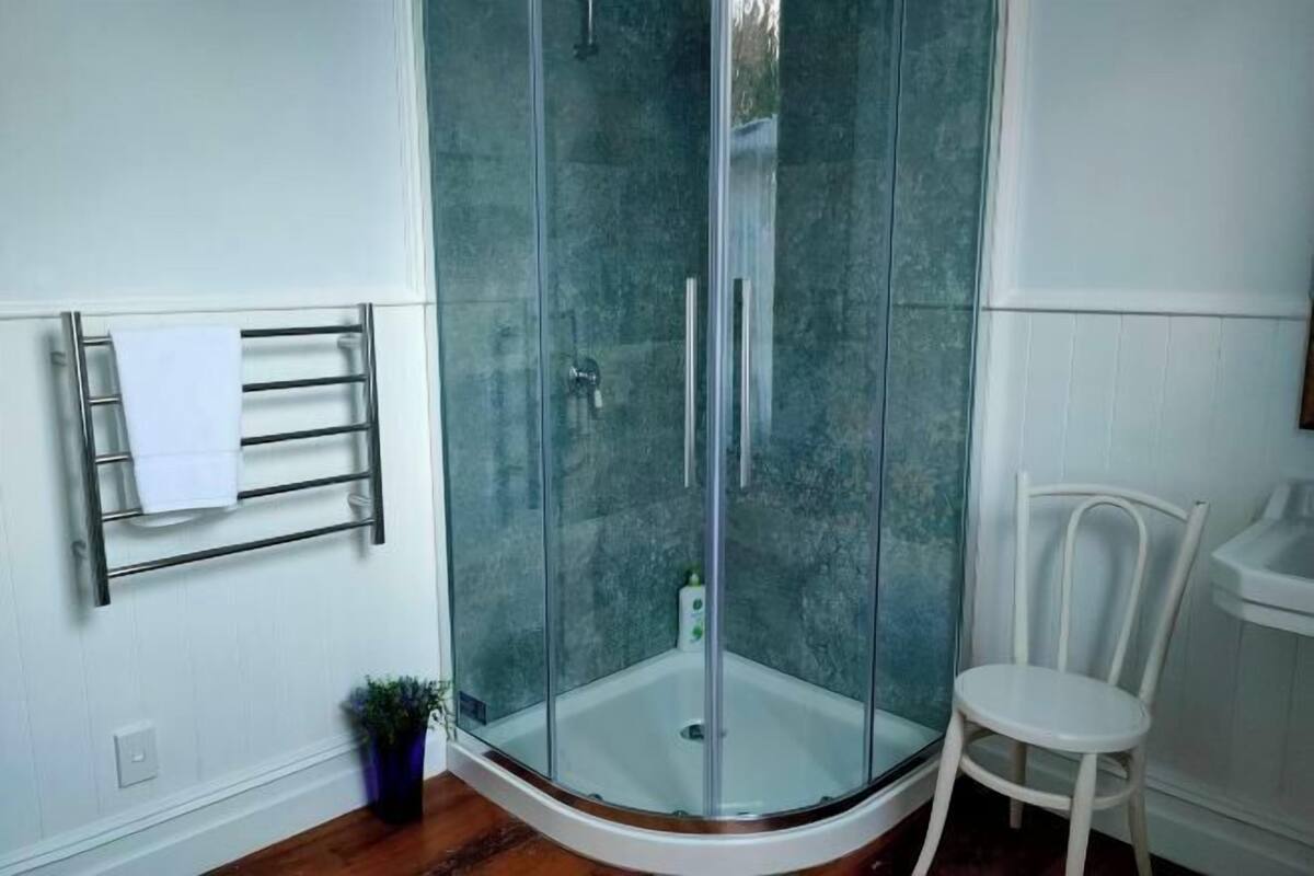 A glass-enclosed shower stall with a white towel rack and chair.