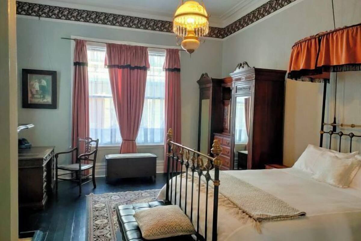 A bedroom with a bed, a desk, a chair, a dresser, and a window with curtains.