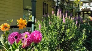 Ein gelbes Gebäude mit einer Veranda, umgeben von verschiedenen Blumen und Pflanzen.