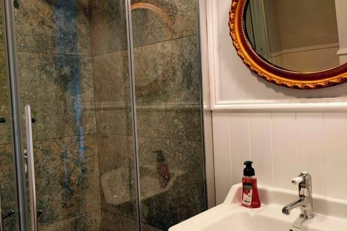 A bathroom with a glass shower enclosure, a white sink with a faucet, and a mirror with a gold frame.
