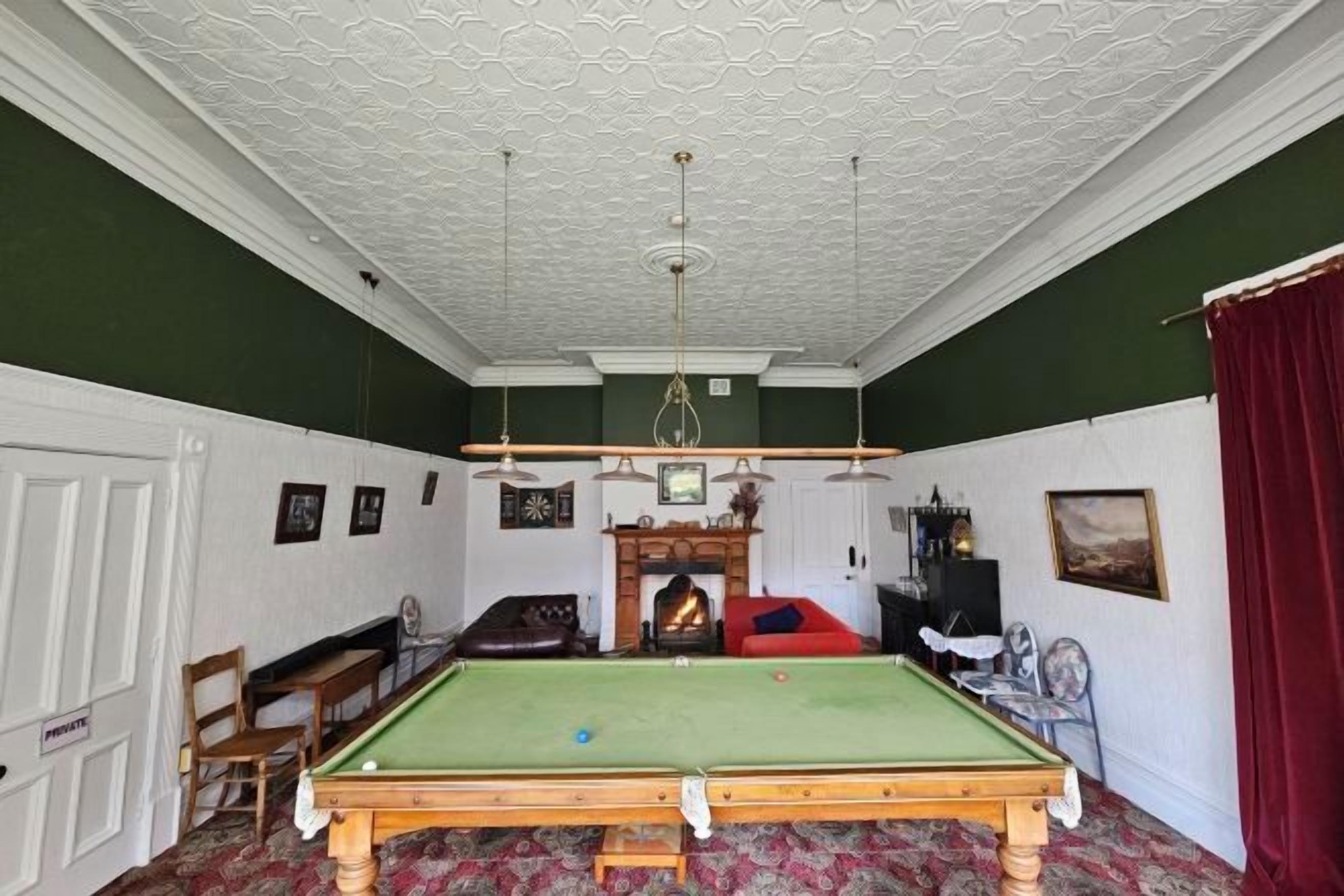 Une salle de billard équipée d’une table de billard, de chaises et d’une cheminée.