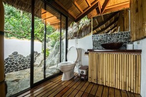 Een badkamer met toilet, wastafel en grote ramen met uitzicht op een natuurlandschap.