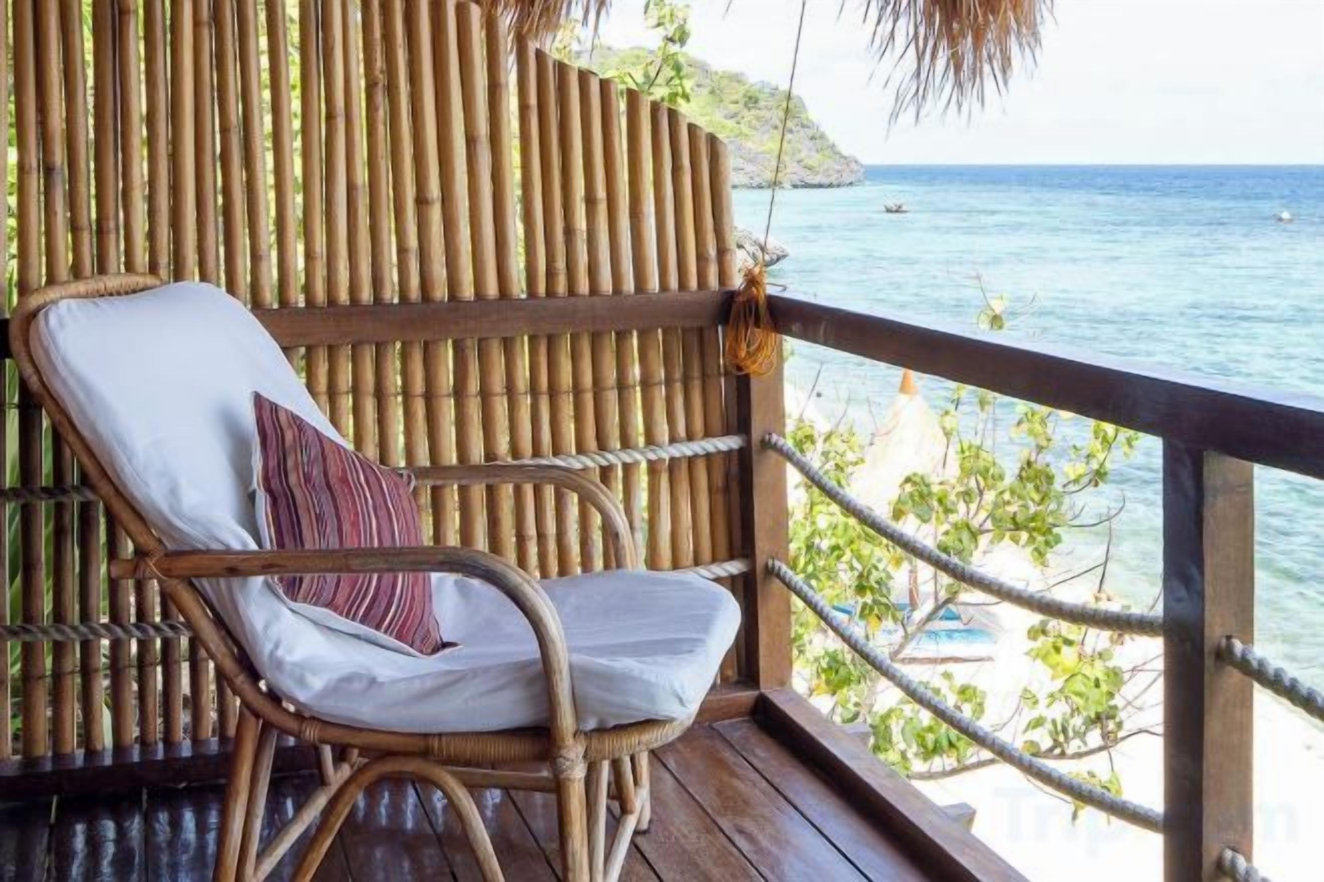 Ein Korbstuhl mit Kissen und Kopfstütze auf einer Holzterrasse mit Blick auf das Meer.