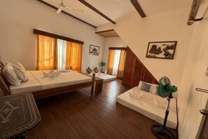 Une chambre avec un lit, un canapé, un bureau et un ventilateur sur pied.