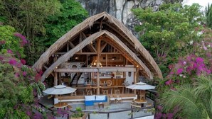 Een houten chalet met rieten dak, buiten zitplaatsen en omringd door weelderige begroeiing.